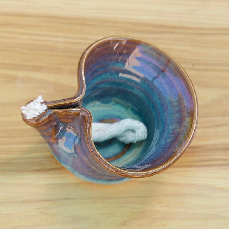 May include: A blue and brown ceramic oil lamp with a white wick. The lamp is handmade and has a unique, wavy design.