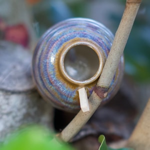 May include: A small, brown ceramic birdhouse with a round opening and a light brown wooden perch attached to a branch.