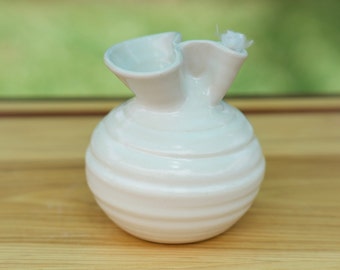 May include: A white ceramic vase with a round body and a ruffled top. The vase has a textured, ribbed surface.