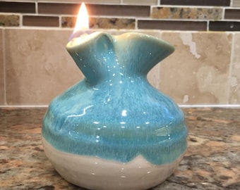 May include: A blue and white ceramic oil lamp with a flame burning inside. The lamp is shaped like a vase with a wide mouth and a narrow neck.