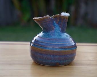 May include: A blue and brown ceramic jug with a wide, round body and a spout. The jug has a textured, glazed finish.