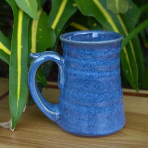 May include: A blue ceramic mug with a speckled glaze and a rounded handle. The mug has a wide base and a slightly flared top.