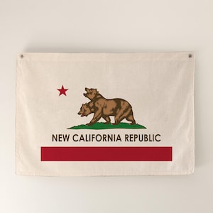 May include: A beige flag featuring the New California Republic emblem. The design includes a brown bear, a red star, a red horizontal stripe, and the text "NEW CALIFORNIA REPUBLIC" in a serif font.