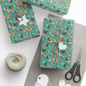 Peut inclure: Des cadeaux emballés avec du papier turquoise orné d'un motif floral et d'oiseaux colorés. Chaque paquet est noué avec de la ficelle et une étiquette blanche. Une pelote de ficelle, des ciseaux et des étiquettes vierges sont également visibles.