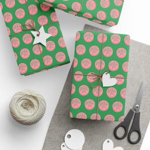 May include: Green wrapping paper featuring a pink circular design with the text "Happy Birthday You." The gifts are tied with twine and have white star and heart-shaped tags. A ball of twine, scissors, and blank tags are also present.