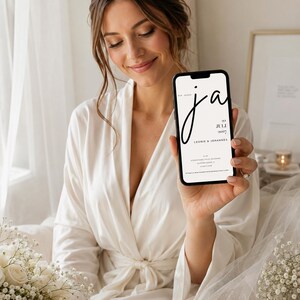 May include: A smartphone displaying a digital wedding invitation with the text "WIR SAGEN ja", "22 JULI 2027", "LEONIE & JOHANNES", and additional event details. The screen features a minimalist black font on a white background.