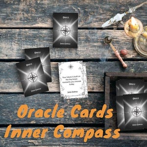 May include: A collection of oracle cards with a compass design, displayed on a rustic wooden surface. The cards feature the words "Oracle" and "Inner Compass." Additional elements include candles, dried flowers, and a wooden box.