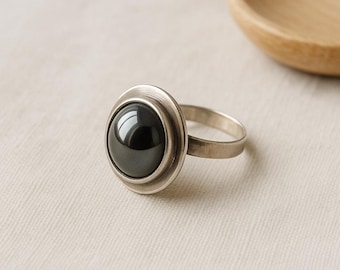 Op de afbeelding: Een zilveren ring met een zwarte hematiet edelsteen gezet in een bezel setting. De ring heeft een eenvoudige band en een ronde, licht verhoogde bezel.