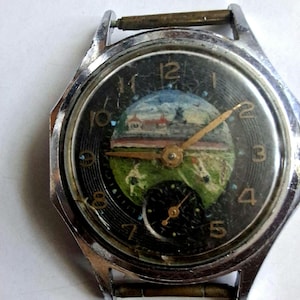 Puede incluir: Reloj de pulsera vintage con esfera negra con pintura de paisaje. El reloj tiene una caja plateada y un pequeño dial de segundos. Las manecillas son doradas y los números están en una fuente clásica.