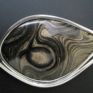 May include: A silver pendant with a black and brown marbled stone set in the center.