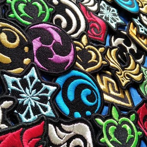 May include: A selection of embroidered patches in diverse shapes and colours. Designs include swirls, geometric patterns, and floral motifs, with gold, green, blue, and red. The patches are on a blue background.