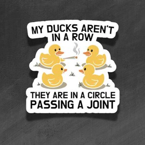 Könnte beinhalten: Ein gestanzter Aufkleber mit vier gelben Quietscheentchen, die im Kreis auf weißem Grund angeordnet sind. Die Enten reichen sich einen brennenden Joint. Der Text lautet: MY DUCKS AREN'T IN A ROW THEY ARE IN A CIRCLE PASSING A JOINT in schwarzer Schrift.