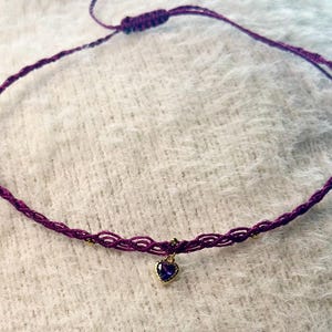 Peut inclure: Un collier ras du cou macramé violet fait à la main. Le collier comporte un petit pendentif en forme de cœur doré avec une pierre précieuse bleue. Le choker est réglable et en cordon violet tressé.