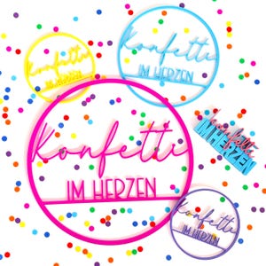 Könnte beinhalten: Eine Sammlung von runden und rechteckigen Wandschildern in leuchtendem Gelb, Blau, Pink und Lila. Jedes Schild zeigt den deutschen Schriftzug "Konfetti IM HERZEN" in einer Kombination aus Schreib- und Blockschrift, umgeben von buntem Konfetti.