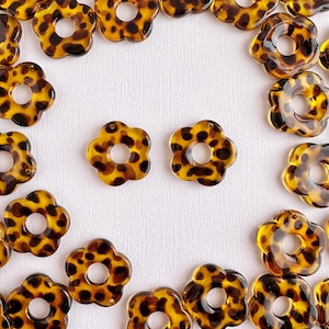 May include: A collection of brown and black flower-shaped beads with a hole in the center. The beads have a leopard print pattern.