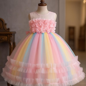 Può includere: Abito multicolore con gonna a strati e corpetto decorato con fiori rosa. L'abito è esposto su un manichino, evidenziando il suo design. La gonna presenta strati di tulle in tonalità pastello, rosa, giallo, blu e verde.