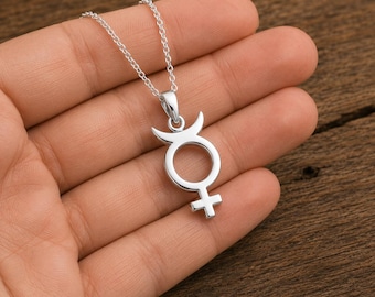 May include: A silver-toned metal pendant necklace featuring the astrological symbol for Mercury. The pendant is suspended from a delicate silver chain and displays a circular center with a cross at the bottom and a crescent moon shape at the top.