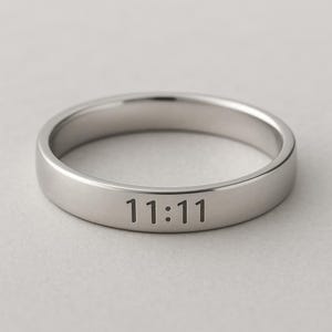 Peut inclure: Une bague argentée avec les chiffres "11:11" gravés. La bague a une surface lisse et polie et un design minimaliste. La bague est probablement en acier inoxydable ou en métal similaire.