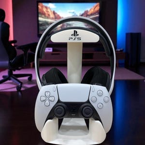 May include: A white gaming headset and controller stand. The stand has a white base with a cradle for the controller and a top section with the PS5 logo to hold the headset. The controller has black joysticks and buttons.