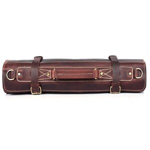 May include: A brown leather roll-up case with a handle and brass buckles. The case is designed to hold and protect knives.
