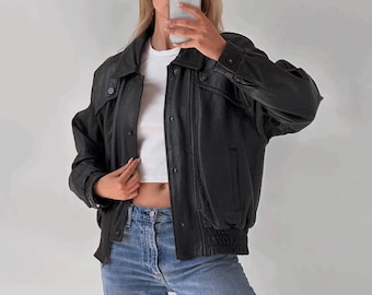 May include: A black leather bomber jacket with a zipper closure and a ribbed waistband. The jacket has a stand-up collar and two flap pockets on the front.