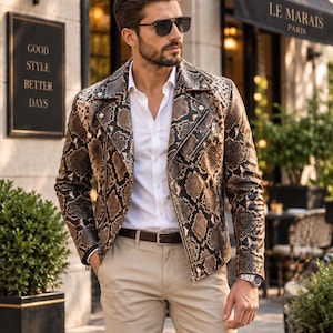 May include: A brown and black snakeskin-patterned leather motorcycle jacket with silver-tone metal zips and snap buttons, worn over a crisp white button-down shirt and paired with beige trousers and a dark brown leather belt.