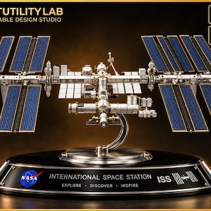 May include: A detailed 3D model of the International Space Station featuring blue solar arrays and a central metallic structure. The model sits on a black base with the NASA logo, the text "INTERNATIONAL SPACE STATION", "EXPLORE DISCOVER INSPIRE", and "ISS".