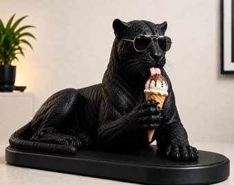 Könnte beinhalten: Eine schwarze Pantherfigur in liegender Position, die eine goldfarbene Fliegerbrille trägt. Der Panther hält ein Waffeleis mit Schokoladensoße und Streuseln, wobei die rosa Zunge herausgestreckt ist, um an der Leckerei zu lecken.