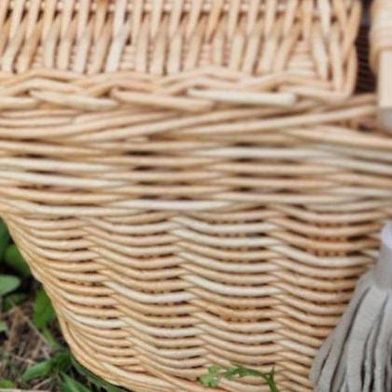 May include: A light tan woven wicker basket featuring a structured lid and a decorative light gray tassel attached to the side. The basket is constructed from natural reed material with a tight, horizontal weave pattern throughout the body.