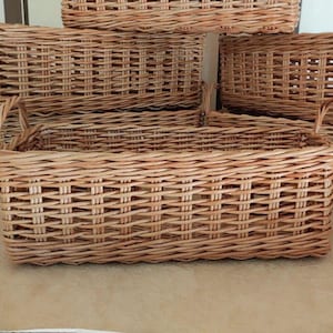 May include: Several rectangular woven wicker baskets with handles. The baskets are light brown and have a woven pattern. The baskets are stacked on top of each other. The baskets are empty.