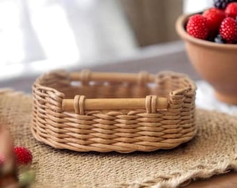 Puede incluir: Una pequeña cesta de mimbre tejida con dos asas de madera. La cesta es rectangular y se encuentra sobre un mantel individual de arpillera. Un cuenco de bayas frescas está en el fondo.