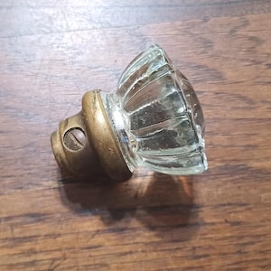 May include: A vintage glass door knob with a ribbed design and a brass base. The knob is clear and has a screw for attachment. The hardware is likely for a cabinet or door.