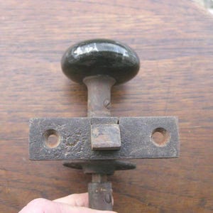 May include: An antique black door knob with a matching rectangular latch. The knob is a rounded oval shape, and the latch has two holes for screws. The metal has a rustic, aged appearance.