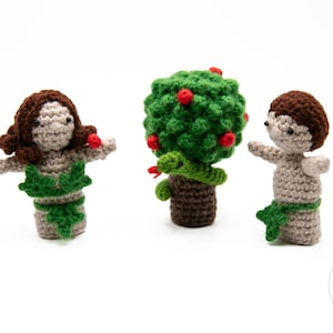 Può includere: Figure all'uncinetto di Adamo, Eva e l'Albero della Conoscenza. Eva ha i capelli castani e una gonna di foglie verdi. Adamo ha i capelli castani e un perizoma di foglie verdi. L'albero ha foglie verdi, mele rosse e un serpente verde.