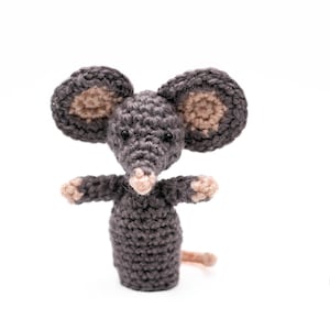 Può includere: Un giocattolo a forma di topo all'uncinetto fatto a mano, nei toni del grigio e del beige. Il topo ha grandi orecchie rotonde, piccoli occhi neri e braccia tese. La coda è di colore marrone chiaro. Il giocattolo è posto su uno sfondo bianco.
