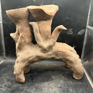 May include: A terracotta sculpture featuring two flared vessels connected by a curved base. The piece has a rough, organic texture and a warm, earthy tone. The sculpture has a unique, abstract design, possibly for decorative purposes.