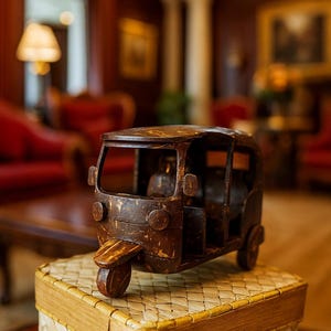 Może przedstawiać: Ręcznie wykonany drewniany model rikszy samochodowej, prezentujący skomplikowane detale. Brązowy pojazd z widocznym wnętrzem stoi na plecionym koszu. Miniaturowy pojazd ma trzy koła i jest przedmiotem dekoracyjnym.