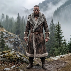 May include: A long brown leather coat featuring a thick grey faux fur collar and cuffs, a waist belt with a buckle, and intricate stitching details. The coat is worn with dark trousers and brown leather boots, while holding a small metal axe.