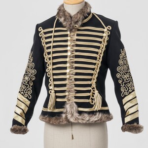 May include: Black military-style jacket with gold trim and decorative rope accents. The jacket features a faux fur collar and cuffs, along with gold embroidered designs on the sleeves. The jacket has multiple buttons down the front.