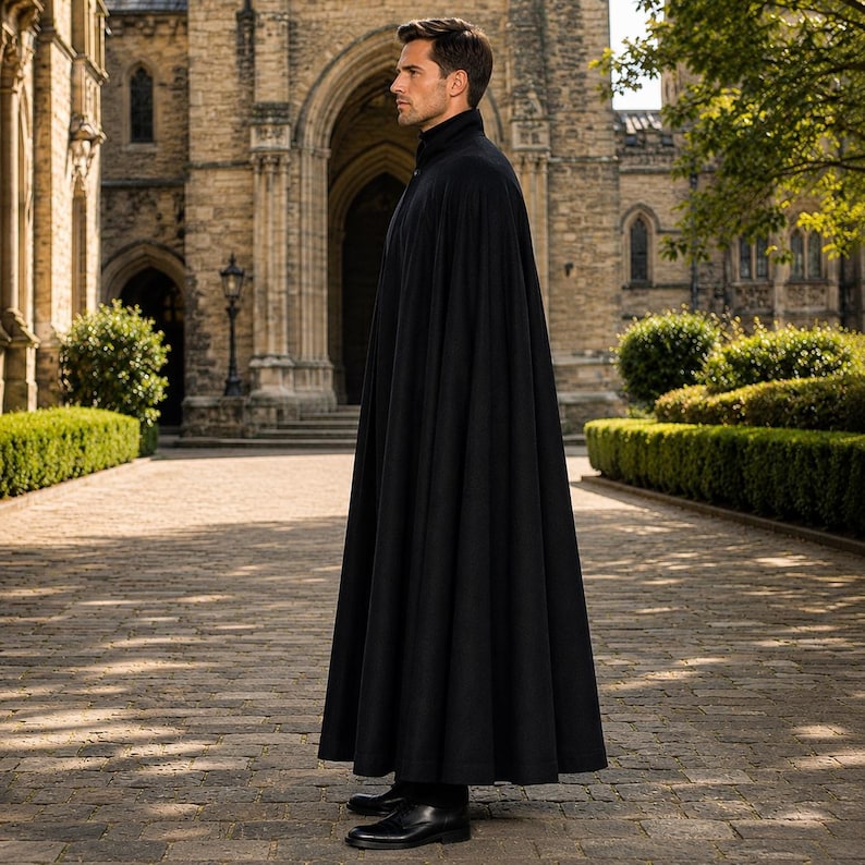 May include: A floor-length black cape with a high collar, worn over dark clothing. The garment features a structured, flowing silhouette that extends to the ankles, with clean lines and a solid, dark fabric finish, shown from a side profile view.