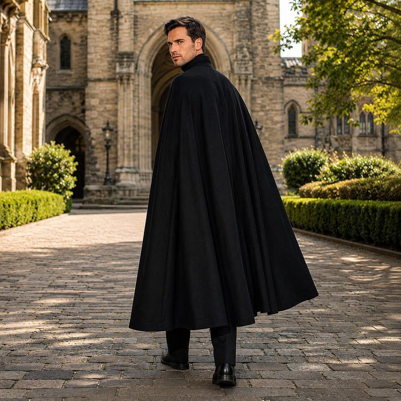 May include: A floor-length black cape with a high collar, worn over dark trousers and black dress shoes. The garment features a structured shoulder design and a full, flowing silhouette that drapes down to the ankles, creating a clean, solid appearance.