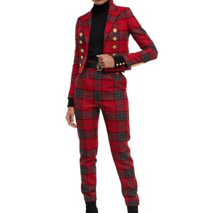 Può includere: Un completo composto da blazer e pantaloni a quadri rossi. Il blazer ha bottoni dorati e una vestibilità corta. I pantaloni sono a vestibilità slim. L'outfit è un'audace dichiarazione di moda.