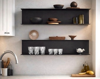 May include: Three-tiered black metal shelves displaying various kitchen items. The shelves hold wooden bowls, plates, decorative vases, and clear patterned drinking glasses. A silver teapot and wooden cutting board are also visible.