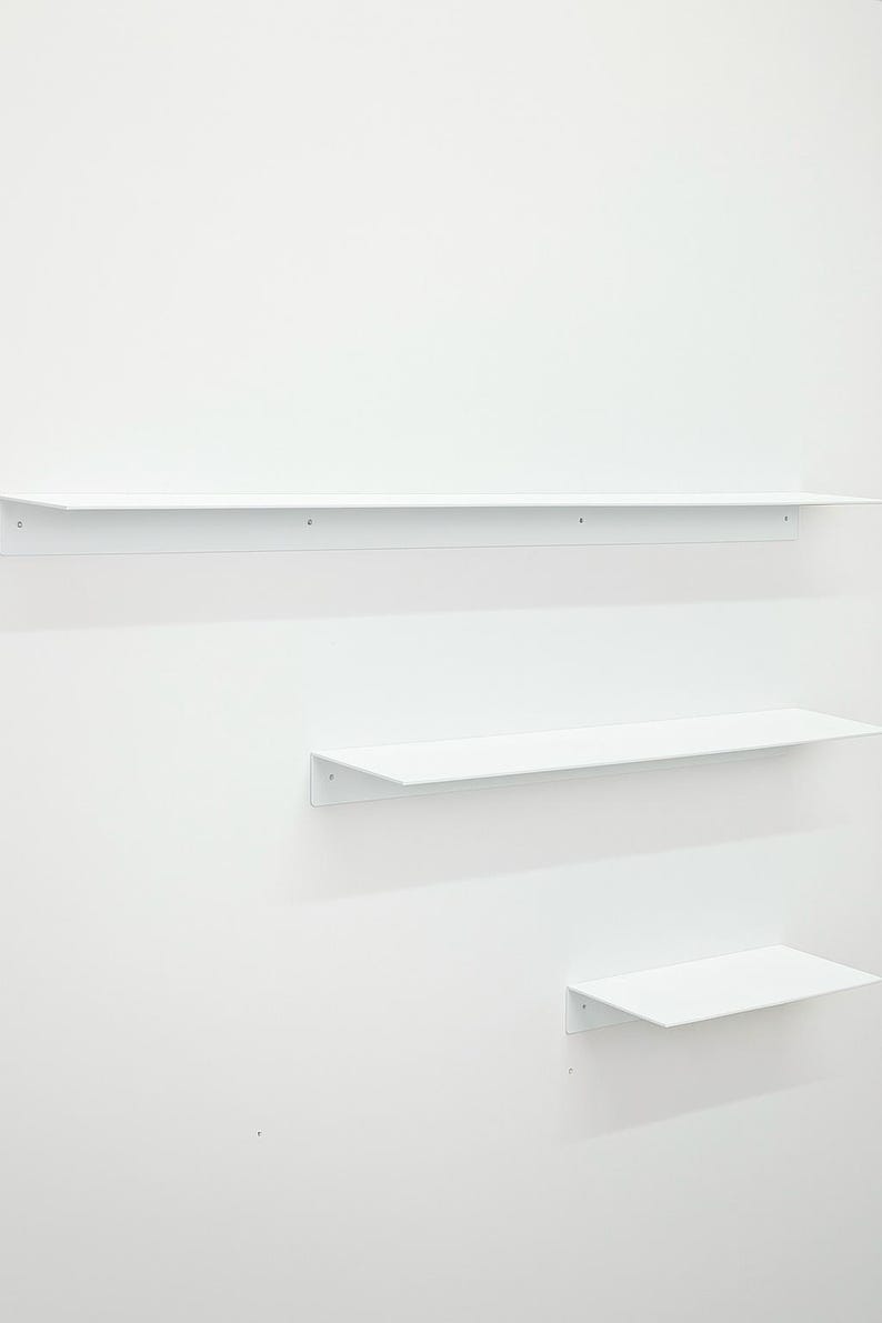 Puede incluir: Tres estantes de pared de metal blanco de longitudes variables montados horizontalmente. Cada estante cuenta con una superficie plana y una placa posterior vertical con orificios para tornillos visibles para su fijaci&oacute;n a la pared.