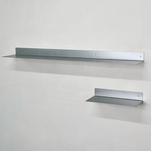 Puede incluir: Dos estantes de pared de metal de color plateado con un acabado liso. El estante m&aacute;s grande es largo y rectangular, mientras que el m&aacute;s peque&ntilde;o es m&aacute;s corto. Ambos cuentan con una superficie horizontal plana y un panel trasero vertical.