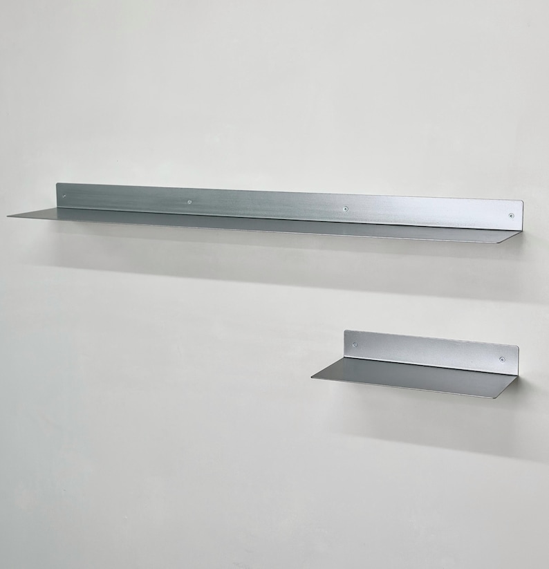 Puede incluir: Dos estantes de pared de metal de color plateado con un acabado liso. El estante m&aacute;s grande es largo y rectangular, mientras que el m&aacute;s peque&ntilde;o es m&aacute;s corto. Ambos cuentan con una superficie horizontal plana y un panel trasero vertical.