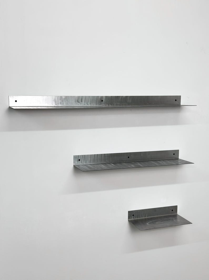 Puede incluir: Tres estantes de pared de metal en forma de L de longitudes variables, cada uno con un acabado plateado cepillado y orificios de montaje circulares preperforados a lo largo del panel trasero vertical para una instalaci&oacute;n segura.