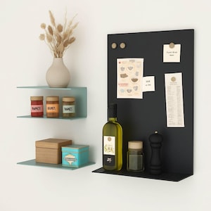 May include: A modern kitchen display featuring a black magnetic board with notes, a green-tinted shelf with jars of spices, a wooden box, and a teal box. A bottle of olive oil and a pepper grinder are also present.
