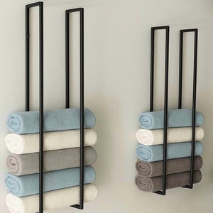 Pode incluir: Dois toalheiros de metal preto montados na parede, cada um com seis toalhas enroladas. As toalhas são em tons de azul, branco e cinza, criando um visual minimalista e organizado para uma casa de banho ou spa.