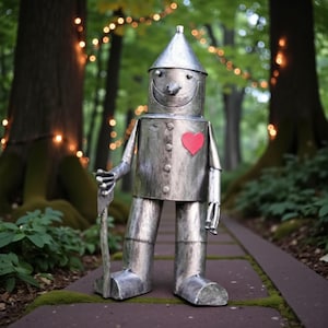 May include: A metallic silver Tin Man sculpture with a red heart on its chest, holding a tool. The figure has a conical hat and a smiling face. The sculpture is standing on a brick path in a forest setting.